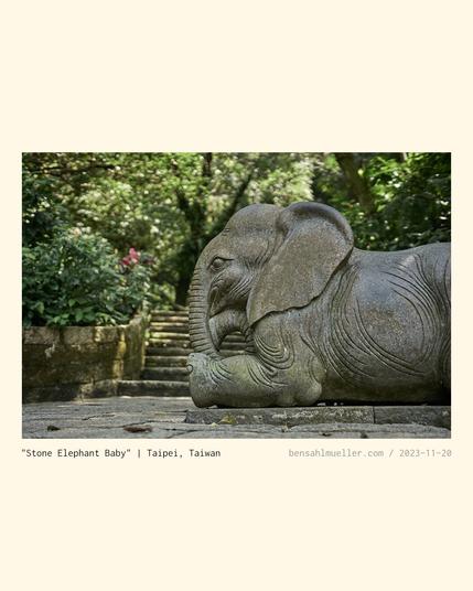 The stone statue of a baby elephant, resting at the side of a stone hiking trail.