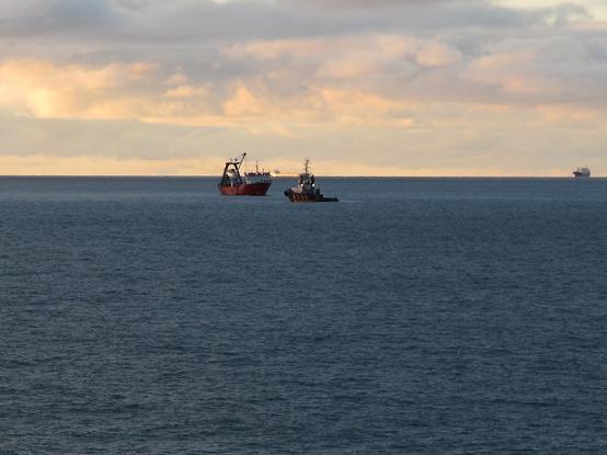 Taucherschiff Vina und Schlepper Wulf 9 nah bei einander im Wrackgebiet. Aufgenommen vom Mehrzweckschiff Mellum aus weiterer Entfernung. Der Himmel ist bläulich-gelblich.