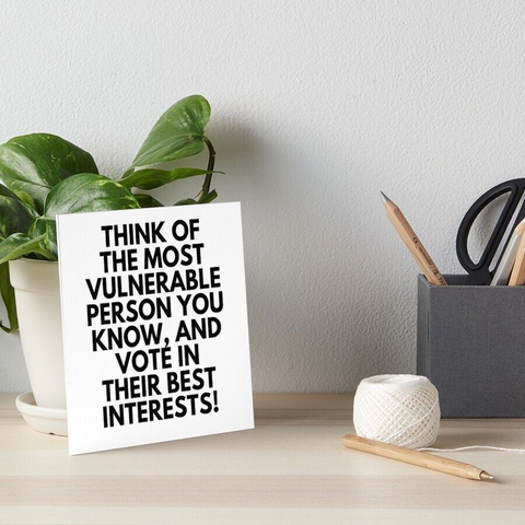 Foto: bureau met plant, kluwen draad, pennenbak, potlood, en tegen de plant aan een bod met de tekst 'Think of the  most vulnerable person you know, and vote in their best interests!'
