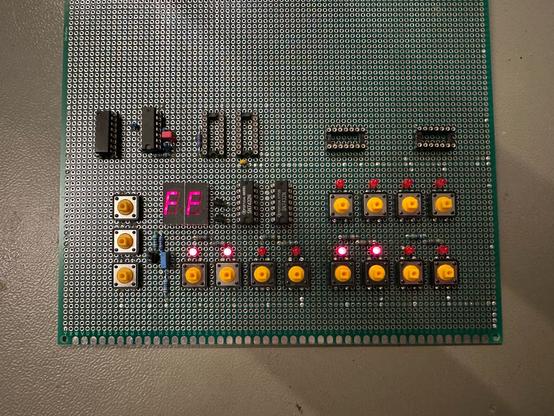 Partially populated veroboard with switches and ICs. Some LEDs light up, and two 7-segment displays show FF.