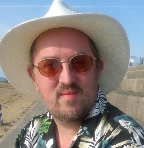 Picture of me from 2013, wearing a sun hat and glasses on the beach.