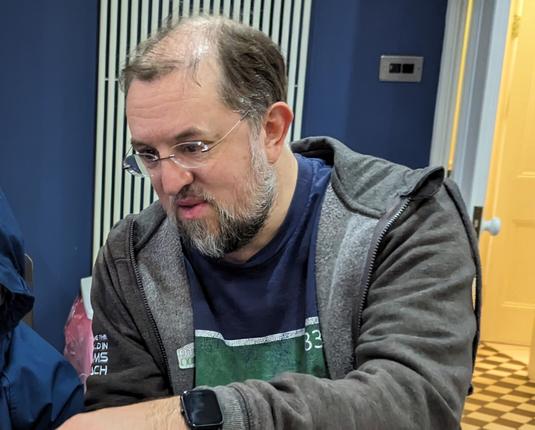 Picture of me from 2023 with considerably less hair wearing a grey Linaro hoodie and showing someone something on the laptop.