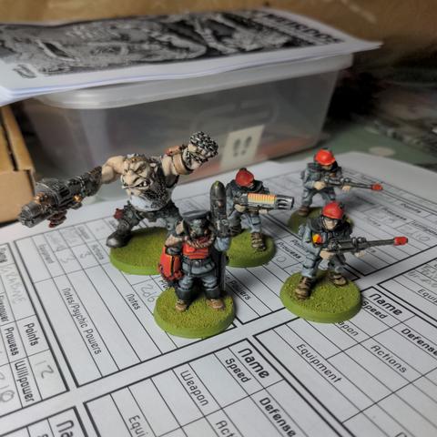 5 hand painted imperial guard miniatures with grey and red uniforms on green bases. A commissar, on ogryn and three guardsmen.
