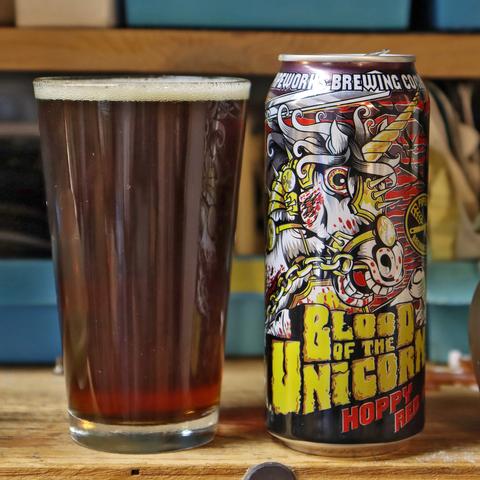 A can of beer stands next to a full beer glass; the liquid in the glass is dark amber.
