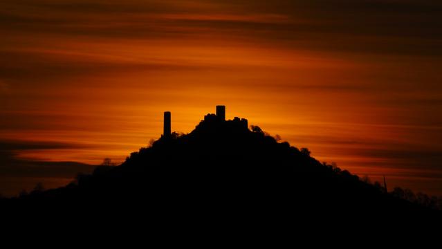 Der Schattenriss eines Berges mit einer Burgruine vor einem Orangefarbenen Himmel