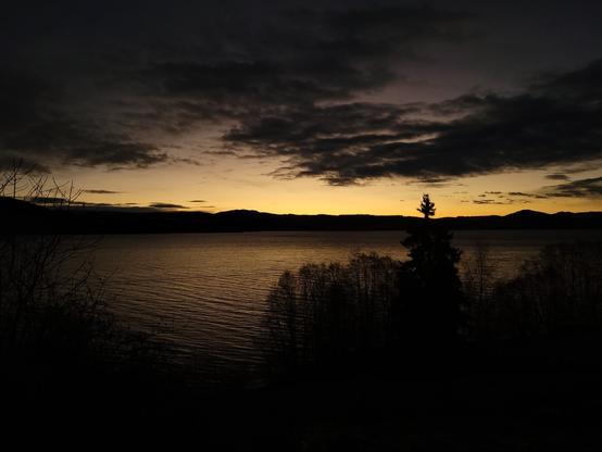 Looking over a lake, this time bathed in a warm yellow colour, a reflection from the yellow sky, awaiting the sunrise. The clouds as well as the trees in the foreground and hills at the horizon are all black against the yellow