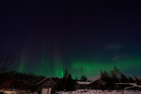A green aurora over some snow covered houses