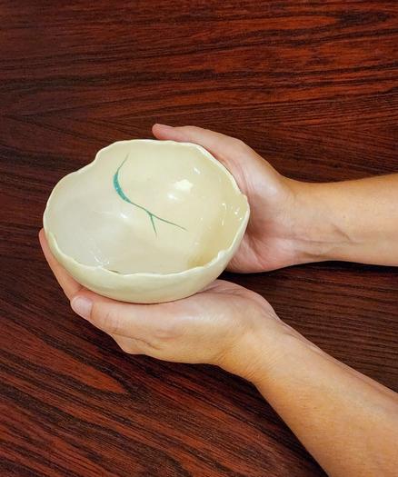 Small porcelain bowl held in two hands with dark wood background table