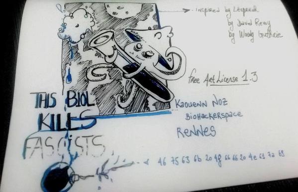 Dessin fait mains sur feuille papier blanc. Un être mi champignon mi poulpe tient en ses tentacules une éprouvette qui relâche un petite nuage depuis lequel son liquide intérieur se répand sous une pluie sombre et battante. Cela forme un tout petit nuage duquel goutte des liquides qui tombent sur « This Biol [ology] Kills Fascists ». Avec quelques stylos qui traient en coin de feuilles À la droite du dessin est écrit Inspired By Lësprëuh, by David Revoy, By Woody Guthrie puis est inscrit la séquence 46 75 63 6B 20 4F 66 66 20 4E 61 7A 69 Dessin sous licence Art Libre 1.3 avec contrib aussi du Kaouenn Noz Biohackerspace