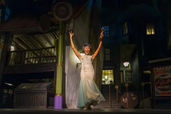 A woman dressed in a flowing white dress on stage with her arms raised.