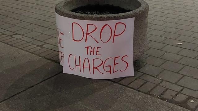 Large handmade sign on a planter outside of Toronto Police Services 52 Division reads:

Drop the charges. 

The sign on the other side of the planter reads:

We won't be intimidated.