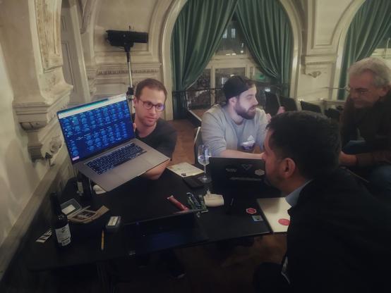Photograph of people at a table, looking at a laptop full of code. Roland, Christian, Hermann and Juan are taking part in a mini-hackathon to look at open source projects and initiatives.