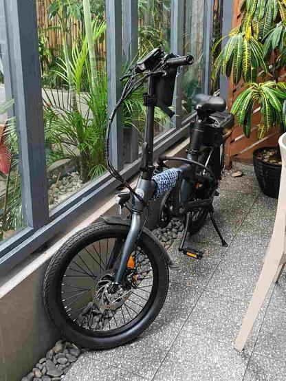 Photo of a dark grey bike parked in a narrow space between a semi-outdoor table and a glass wall
