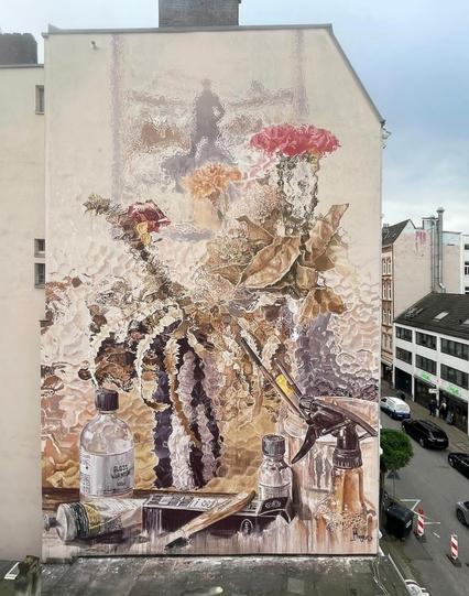 Streetartwall. A huge mural (200 m²) with a still life was sprayed/painted on the exterior wall of a modern four-storey building. Painted almost fleetingly in pastel colors, the result is a bouquet of flowers with pink blossoms and brown stems that appears to have been painted on wavy frosted glass. In front of it are painting utensils: glass bottles, spray bottles, paint and brushes. A painting by Caspar David Friedrich (the "Wanderer") can be seen in the background.
Info: The painting "Wanderer above the Sea of Fog" (around 1817) is the most famous and most copied painting by Caspar David Friedrich, whose 250th birthday will be duly celebrated in 2024. From December 15, 2023 to April 1, 2024, the Kunsthalle Hamburg will be showing around 70 of his paintings, including numerous iconic key works and around 100 drawings.