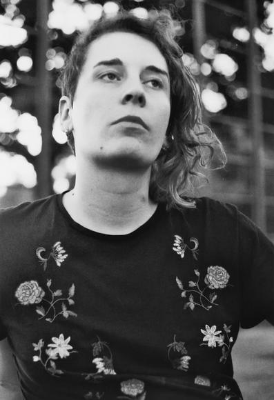 Black and white portrait of Zora, a white trans woman in her 20s with curly hair, sitting outside in the evening light looking relaxed