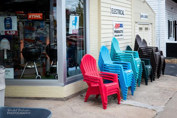 Stacks of plastic chairs in red, blue, green, brown, and black sit in front of a hardware store