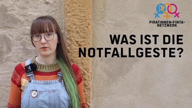 Ich mit Latzhose und bunten Pulli, rotbrauner und grüner langen Ponyfrisur und Brille vor einer grob verputzen Wand. Rechts neben mir das Logo des Piratinnen+FINTA-Netzwerkes und die Worte: "Was ist die Notfallgeste?"