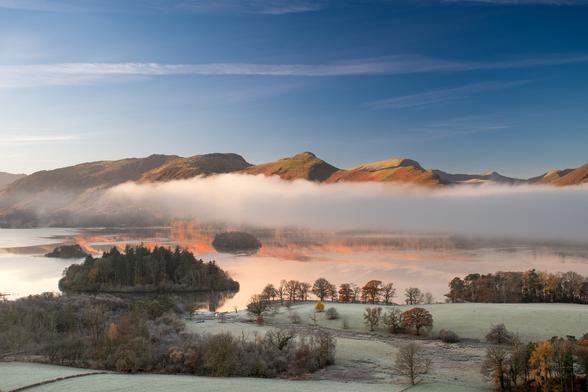 Lake with autumn coloured mountains rising behind.  Cloud inversion floating over the lake in a single layer.
