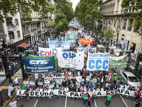 A large crowd marches down a street while holding banners