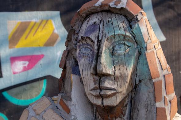 color photograph, portrait format. a wooden sculpture, a portrait head, wrapped in a brick coat. painted walls in the background. santiago de chile, august 30, 2023.