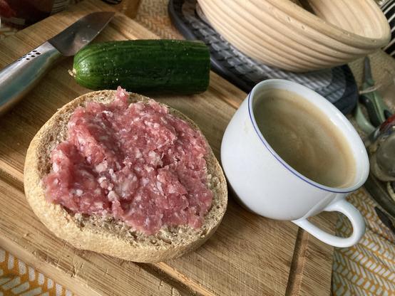 Americano, ein Stück Gurke, Zwiebelmett auf nem Dinkelweckle, natürlich selbst gebacken und ein kleines Messer auf einem Vesperbrett aus Holz.