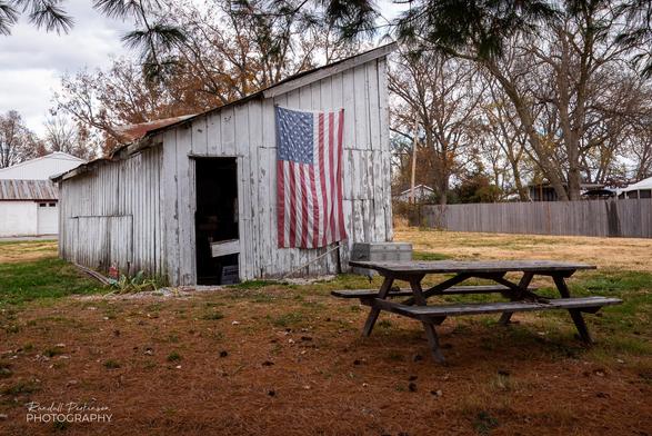Picnic table sits in front of weathered white shed with an American flag hanging on its side.