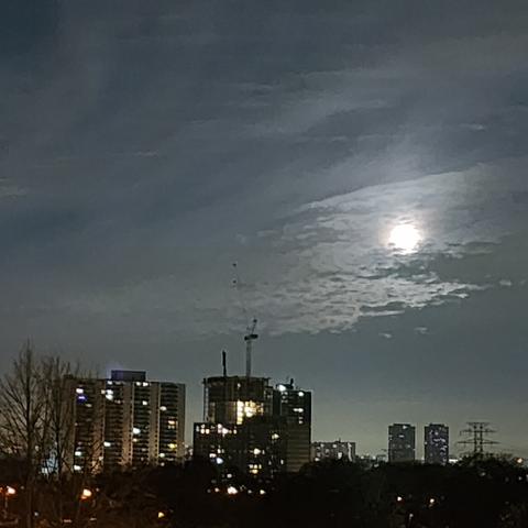 Full moon with clouds. High rises in the foreground.