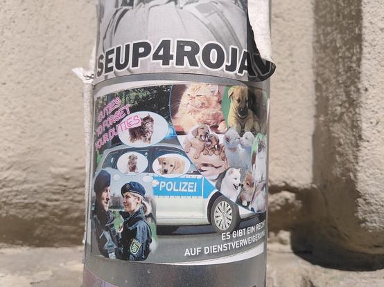 An einer Regenrinne kleben mehrere Aufkleber. Oben steht Rise up 4 Rojava.
Unten sind Ein Streifenwagen und zwei Polizistis abgebildet. über den Köpfen der Cops schweben Denkblasen mit süßen Katzen und Hundewelpen. Dabei steht: "Cuties to forget your duties. Es gibt ein Recht auf Dienstverweigerung.