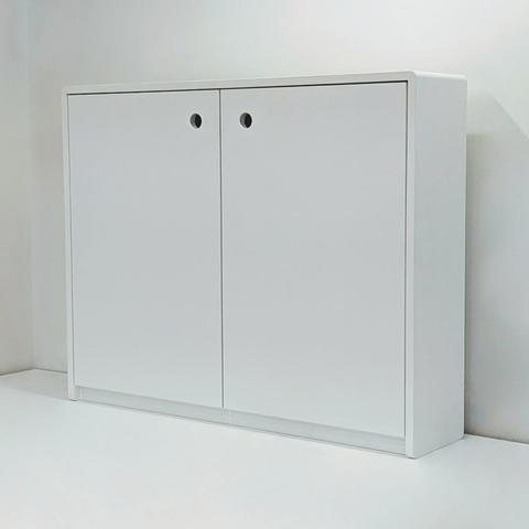 A small storage cabinet painted white. It has two doors that have holes cut out at the corners that act as handles.