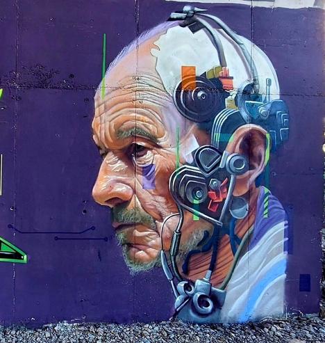 Streetartwall. A great portrait of a semi-artificial being from the Star Trek universe was sprayed/painted on a street wall. The background is purple. One half of the face of the character of Captain "Jean Luc Picard" from the Starship Enterprise (Star Trek) is equipped with futuristic implants made of processors and cables. Picard is an older gentleman with wrinkles, a short gray beard and a half bald head. The mural is supposed to show the captain transformed into a Borg, thus becoming "Locutus".
Info: "Locutus of Borg" is the Borg name of Captain Jean-Luc Picard after he was assimilated in 2366.