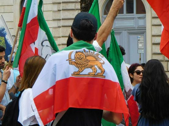 a boy at the march  seen from behind  wearing the iranian flag  as a foulard  on his back