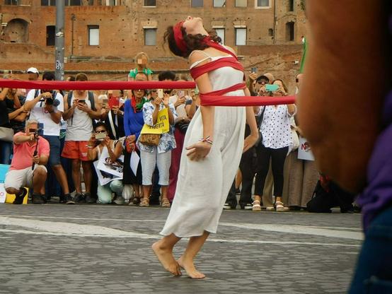 the dancer  now  trying to escape the tape that is now  tightening her  to her chest as well .    head is raised upwards ,  eyes still covered .   ( notice how she danced for several minutes while totally blinded!)
 (( .. the performance continued  ,  and she finally freed herself  in the end ))