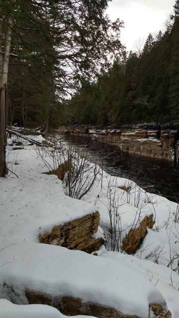 Une rivière bordée de végétation, en hiver. Les bords rocheux sont érodés en parois verticales.