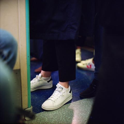 A picture of a person’s sneakers, a white pair of Adidas Stan smiths, in amongst other feet ￼