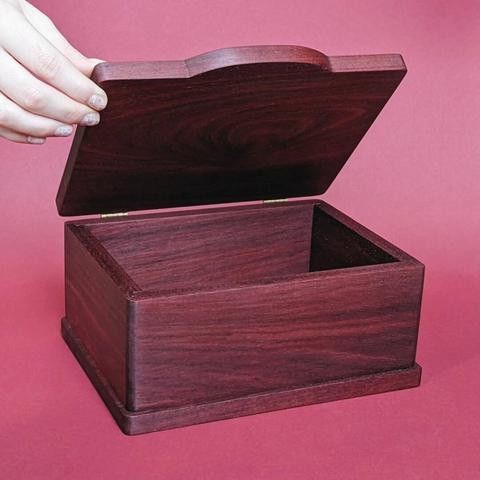 A bloodwood keepsake box with a hand keeping the lid open against a red background.