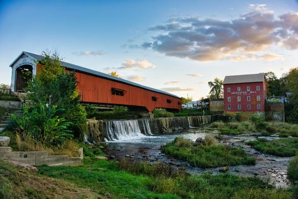 Covered bridge over a waterfall with a grist mill to the right. Near sunset with colorful clouds