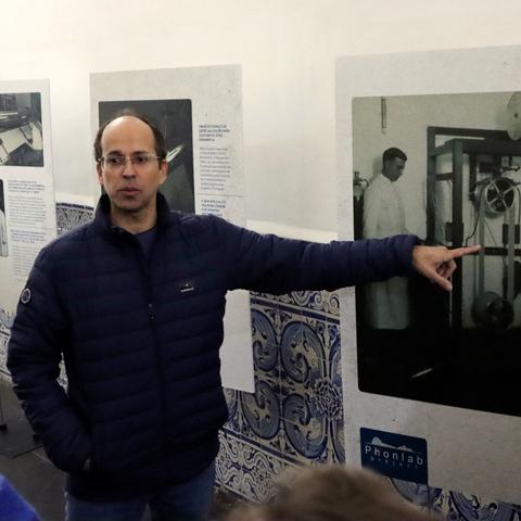 Quintino Lopes a apontar para uma fotografia de um instrumento do laboratório de fonética experimental de Coimbra