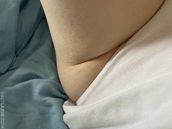 A closeup of the side of Lucy's hip and thigh featuring the natural fold of skin as she sits on light blue fabric , wearing white ribbed underwear and a white shirt.