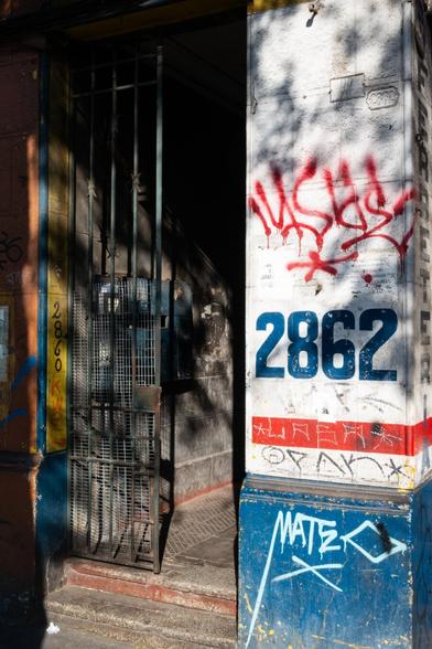 color photograph, portrait format.  a house entrance in the sun. fences, shadows, santiago de chile.