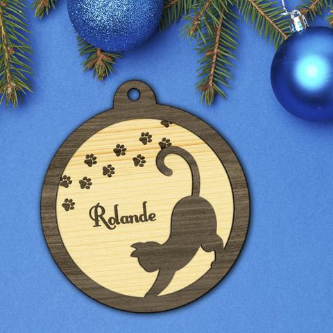 Boule de Noël en bois découpé et gravé représentant la silhouette d'un chat qui s'étire et de petites traces de pattes. La boule est personnalisée avec le prénom de votre choix. A retrouver dans notre boutique en ligne : ernestine-etcie.fr