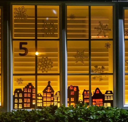 A white window with the cut outs of snowflakes and silhouette houses, each with bright windows. One of the windows decorated for Sustainable St Alban's Festive Streets.📸 Picture: Sustainable St Albans/Cam Ross