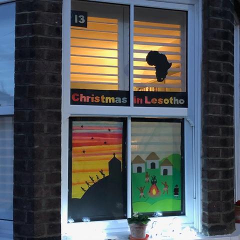 This window depicts Christmas in Lesotho, a map of Africa showing the country in the south, a beautiful sunset and people in a village dancing around a fire. 📸 Picture: Sustainable St Albans