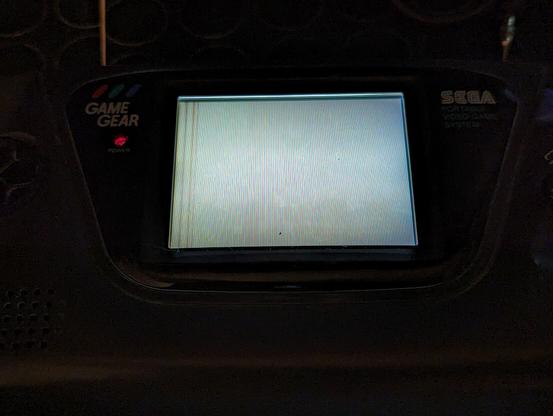 A Game Gear, turned on. But shows a whitish screen with a few darker vertical bars on the left