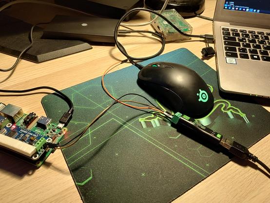 a raspberry pi with a can shield attached on the left. it is hooked up to a CAN to USB connector on the right. they are placed on a desk with mouse, mouse pad and laptop.
