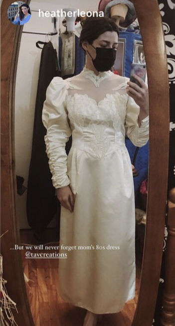 Woman wearing a vintage wedding gown in ivory satin with gathered leg of mutton sleeves and lace detailing on bodice up to a mesh yoke and lace collar