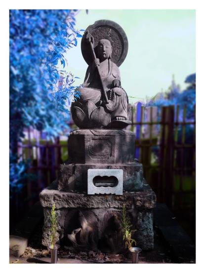 Picture taken of a stone statue of a sitting skinny Buddha in front of some trees. I've changed the colors to make everything take a blue and violet hue. I've also messed with what's in focus to give it an erie effect.