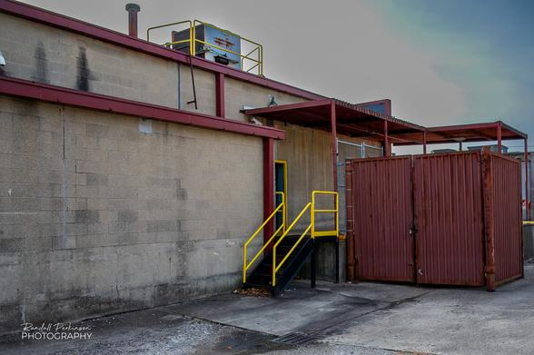 Yellow Railings are on the stairs and loading dock and around the roof air conditioner at the back of a concrete block retail shopping building.