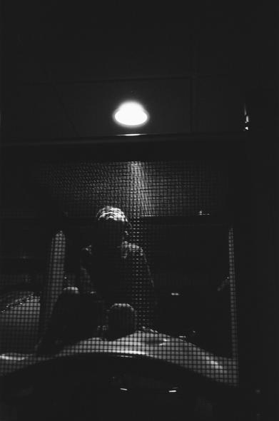 A black and white photograph of a male human child looking up into a light above him.