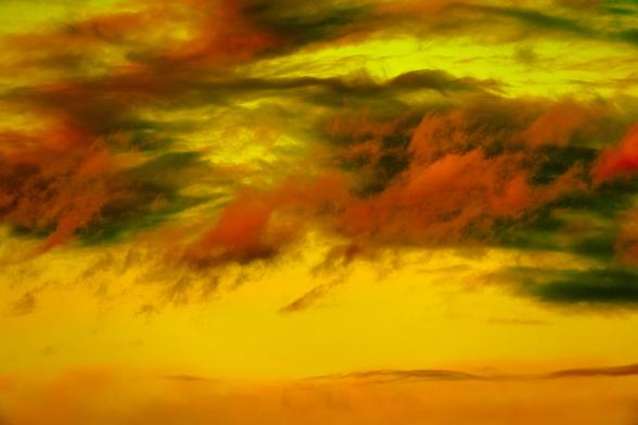 Ephemeral reddish-orange clouds with deep green shadows condense and evaporate in the wind across a neon yellow sky.