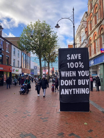 City center with cars excluded, brick paving, trees, and folks walking about. A large sign reads: "Save 100% when you don't buy anything."